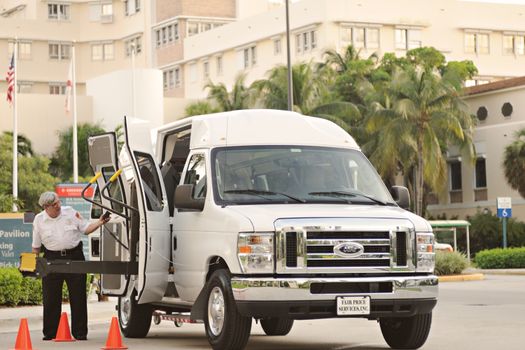 Van with wheelchair lift and driver assisting, located outdoors near a hospital or medical facility.