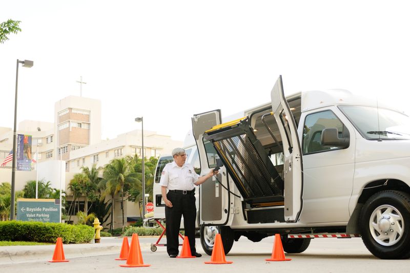 A security guard operates a wheelchair lift on a van outside a medical facility.