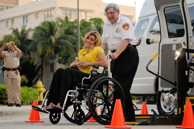 A woman in a wheelchair is being helped onto a vehicle with a lift service.