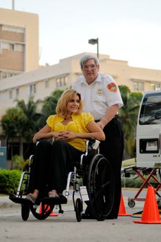 A security guard assists a woman in a wheelchair outdoors near a medical facility.