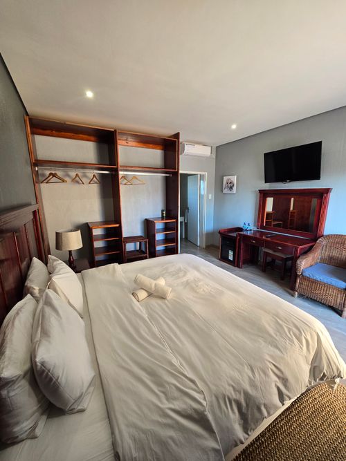 Free Spacious hotel room showcasing a king-size bed, TV, and wooden furniture. Stock Photo