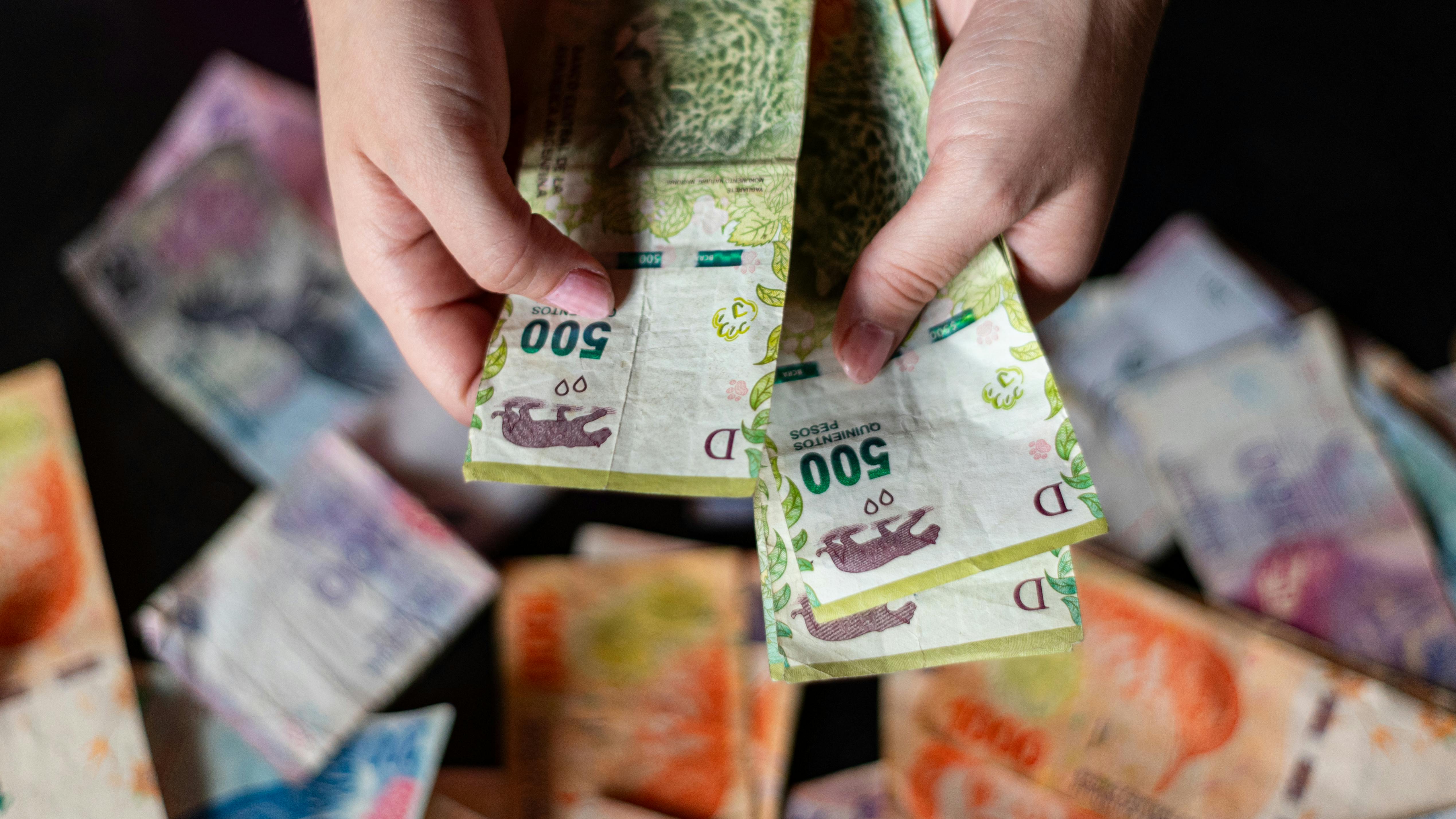 Hands holding Argentine peso banknotes, showcasing currency design and details.