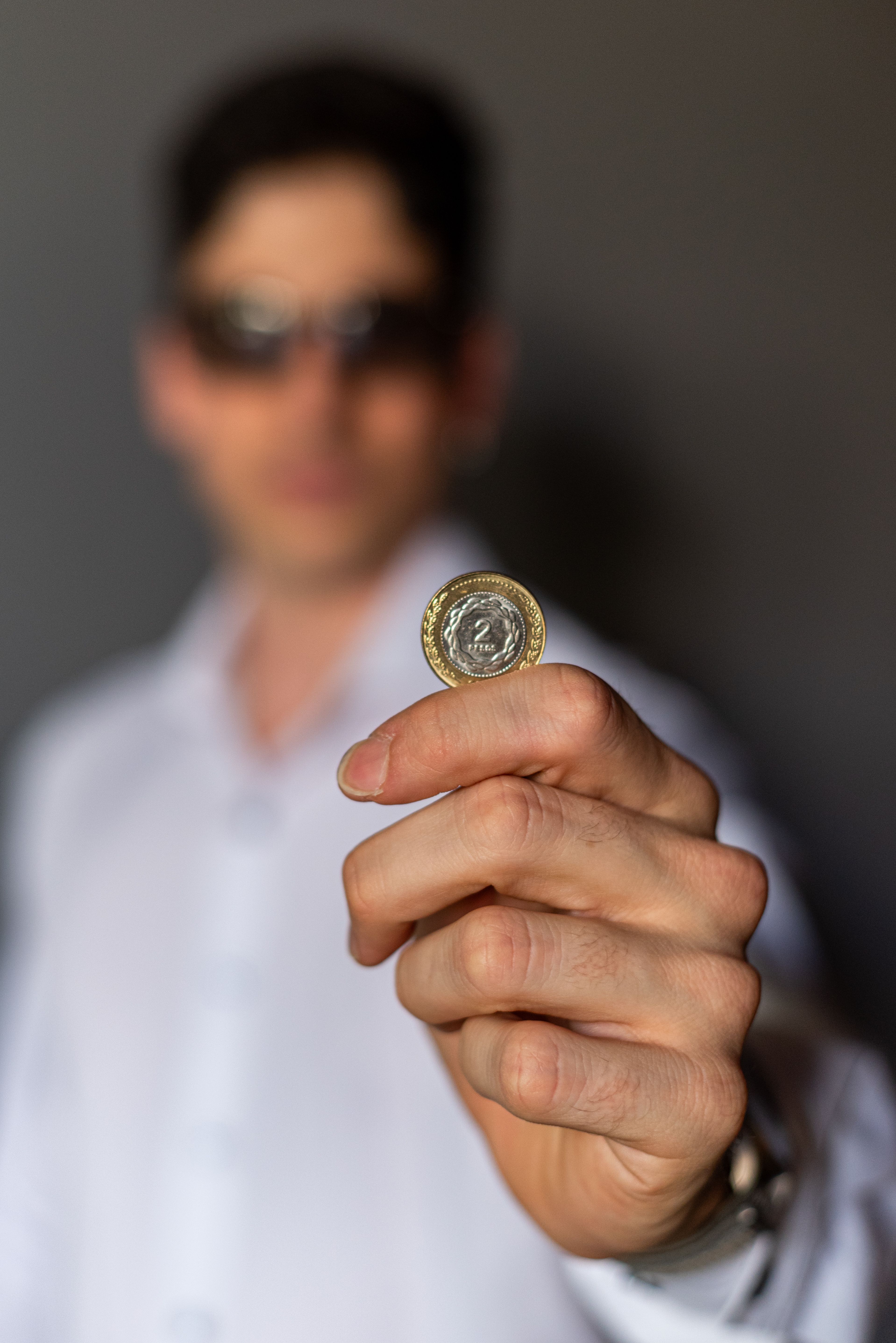 Blurry background with focus on Argentine peso coin held by a man in a white shirt.