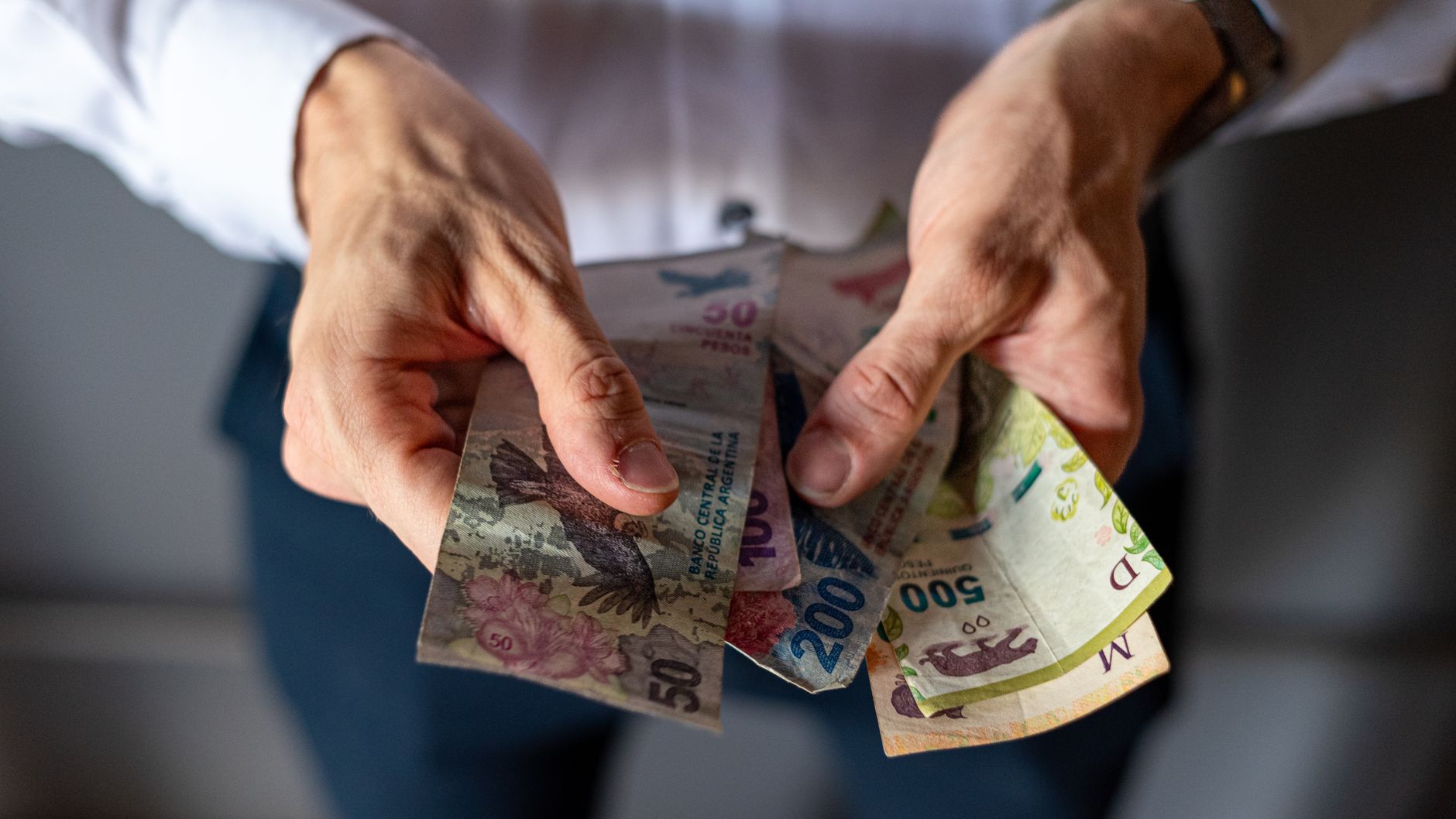 Closeup of hands holding various Argentine peso banknotes, depicting a finance management system concept