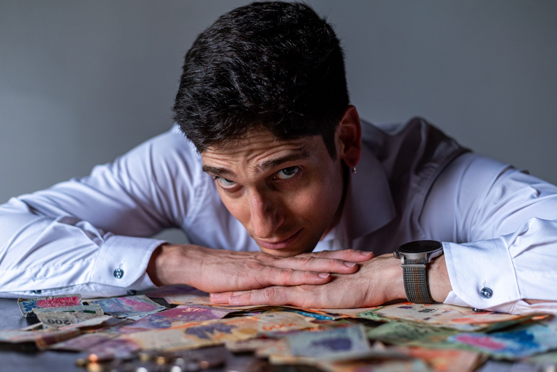 Young man thoughtfully gazes over a collection of Argentine currency notes, symbolizing financial reflection.