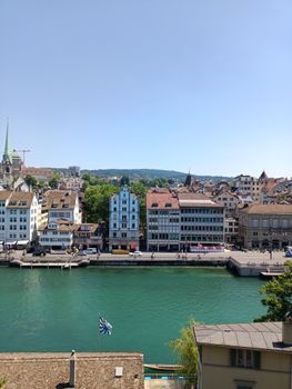 A picturesque view of Zurich's historic waterfront with charming buildings along the river under a clear blue sky.