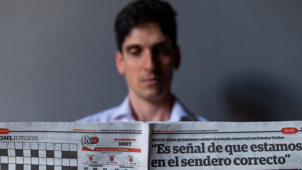 Man holding a Spanish newspaper with headline and date visible, indoors.