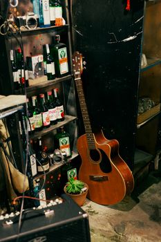 An intimate view of a bar corner showcasing an acoustic guitar and a shelf stocked with various bottles.