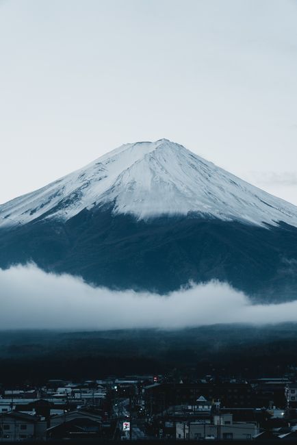 Snow-capped Mount Fuji stands majestically at dusk, enveloped in mist. A serene winter scene in Japan.