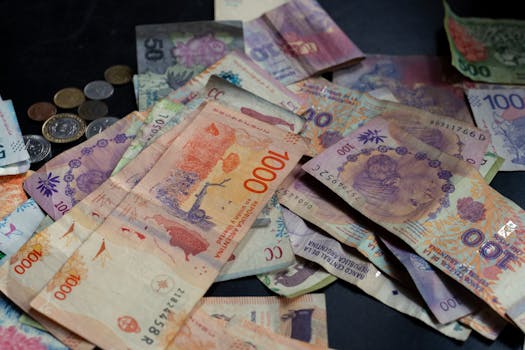 Pile of Argentine peso banknotes and coins scattered on a table in Buenos Aires, Argentina.