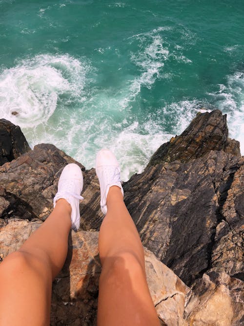 Legs of Person sitting on Cliff Towering over Disturbed Sea