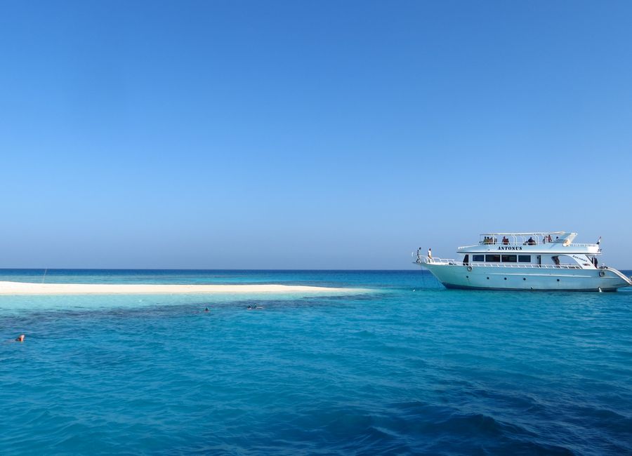 A scenic view of a luxury yacht by a pristine, sandy island in Egypt's vibrant blue waters.