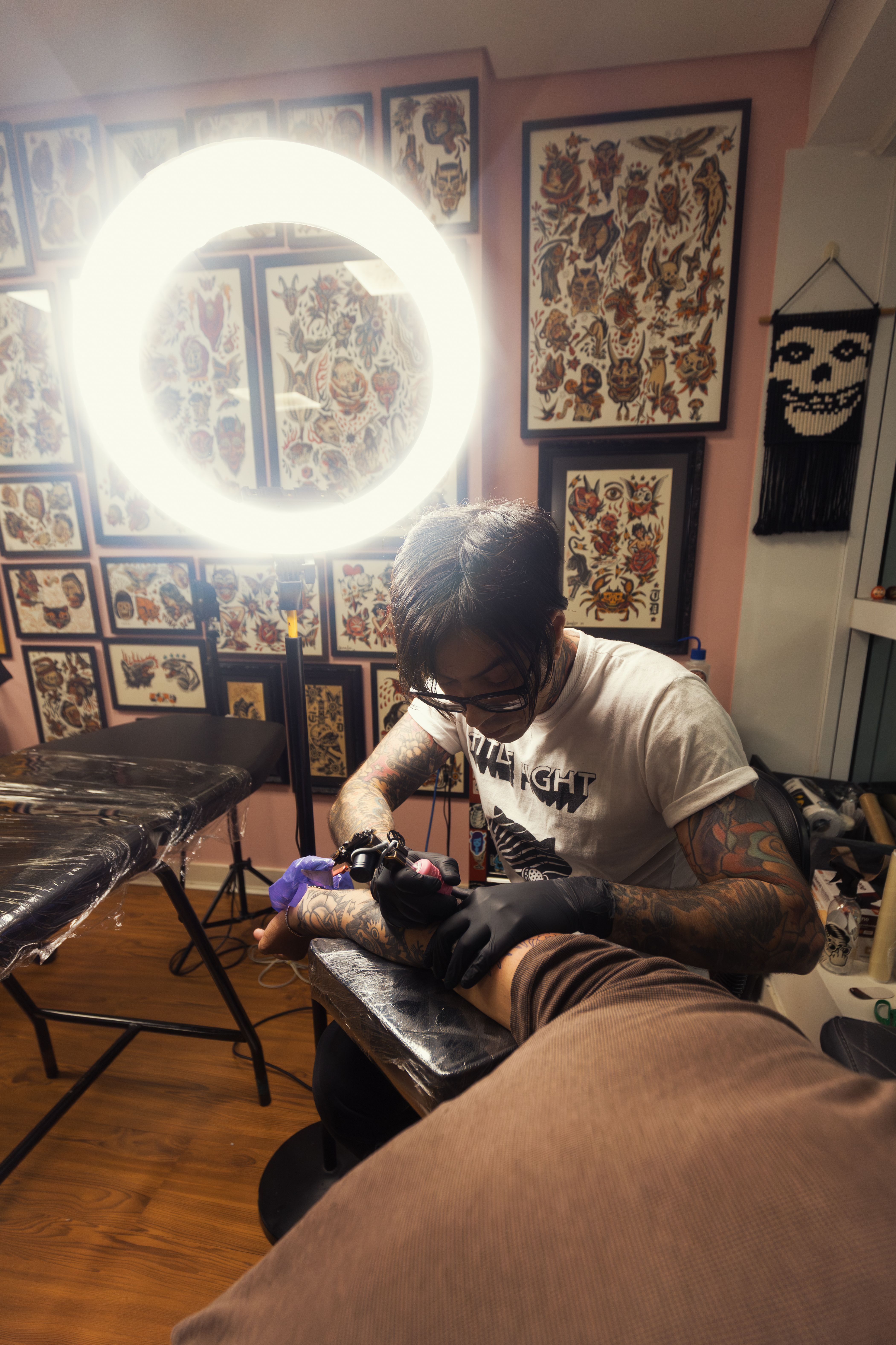 A tattoo artist focused on creating a design on a client's arm in a busy studio.