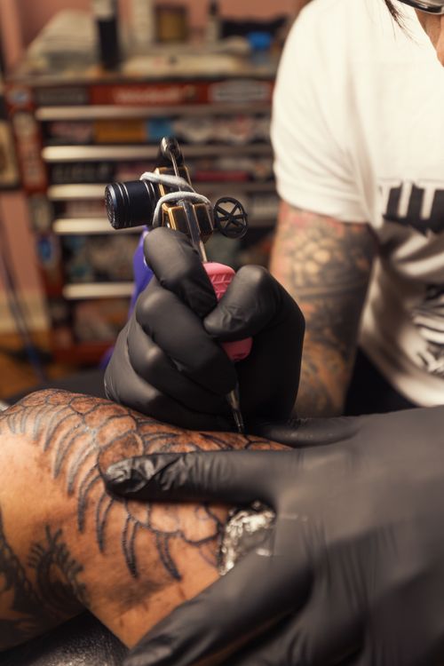 Free Tattoo artist skillfully working on an arm with an intricate design in a tattoo studio. Stock Photo