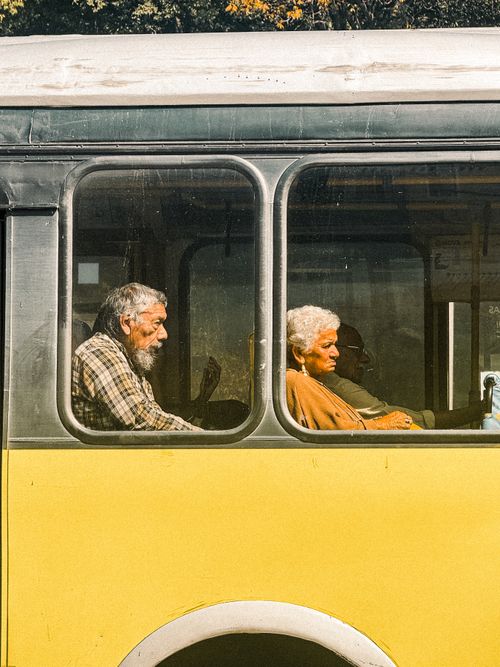 Free Elderly couple seated in a yellow bus, captured in warm daylight. Street photography moment. Stock Photo