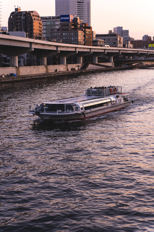Free A tranquil scene of a boat navigating the Sumida River in Tokyo during sunset. Stock Photo