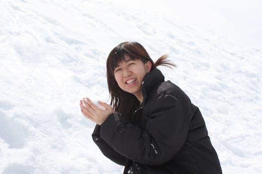 Smiling woman in black coat clapping hands in snowy landscape during winter day.