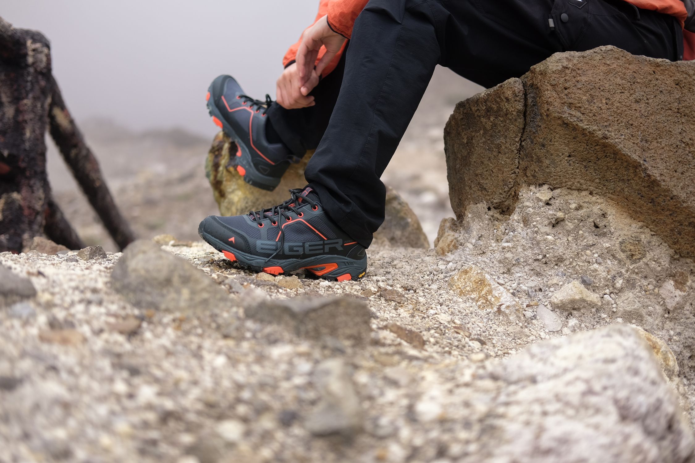 A hiker resting on a rock wearing trekking boots during a mountain hike in West Java, Indonesia.