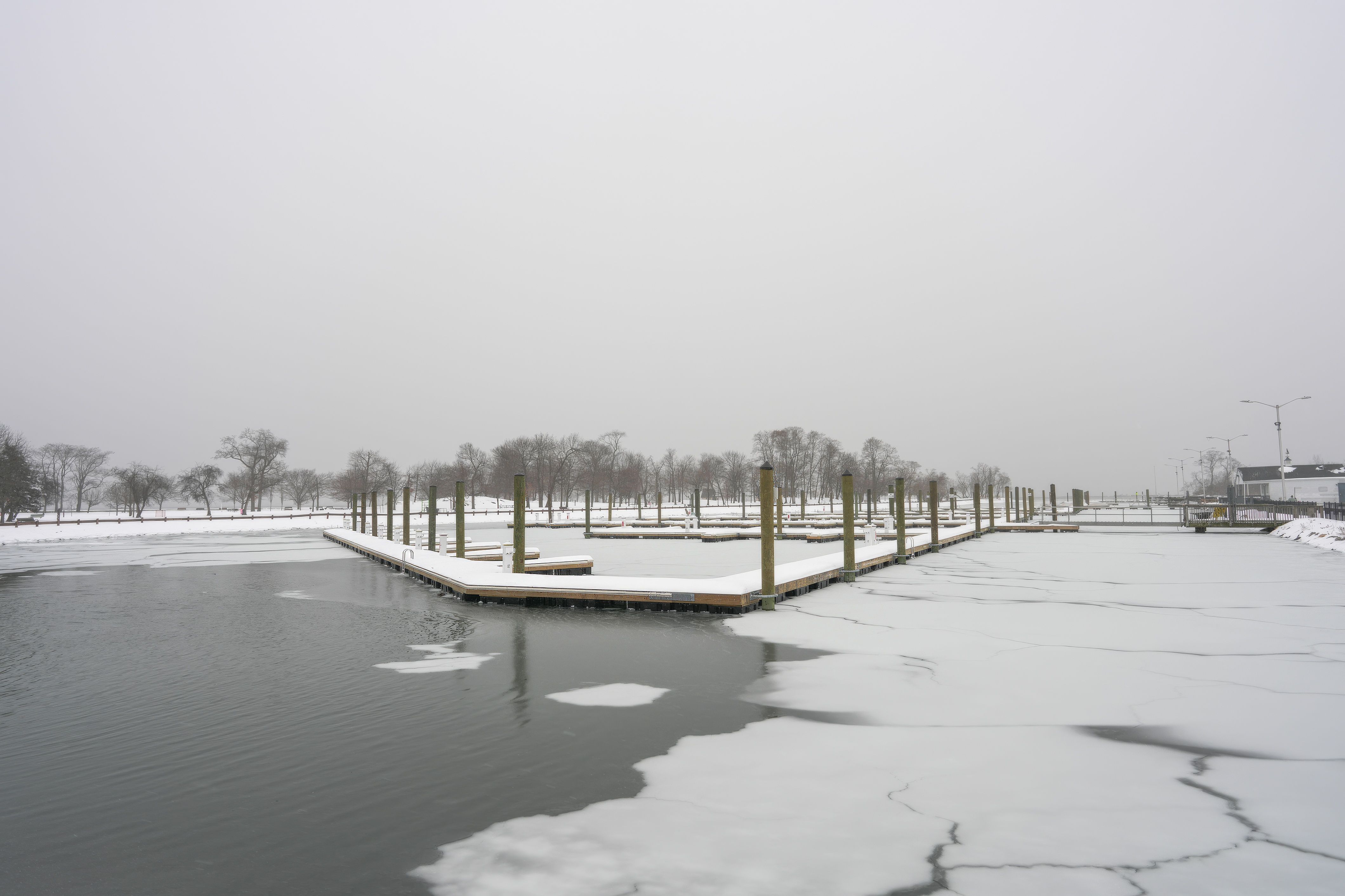 A serene winter scene of an icy harbor with snow-covered docks under a gray sky.