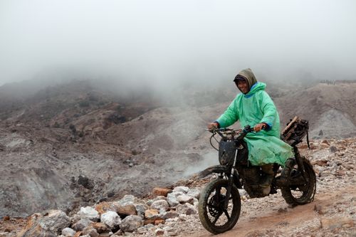 Free A man in a green poncho rides a motorcycle through a foggy volcanic landscape in West Java, Indonesia. Stock Photo