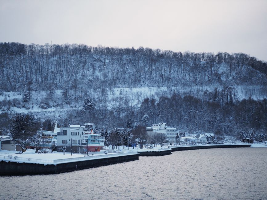 Serene winter landscape of Lake Toya in Hokkaido, Japan with snow-covered trees and buildings.