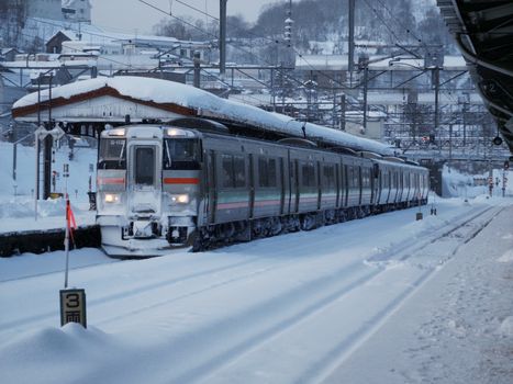 A train covered in snow at a station during winter, surrounded by snow.