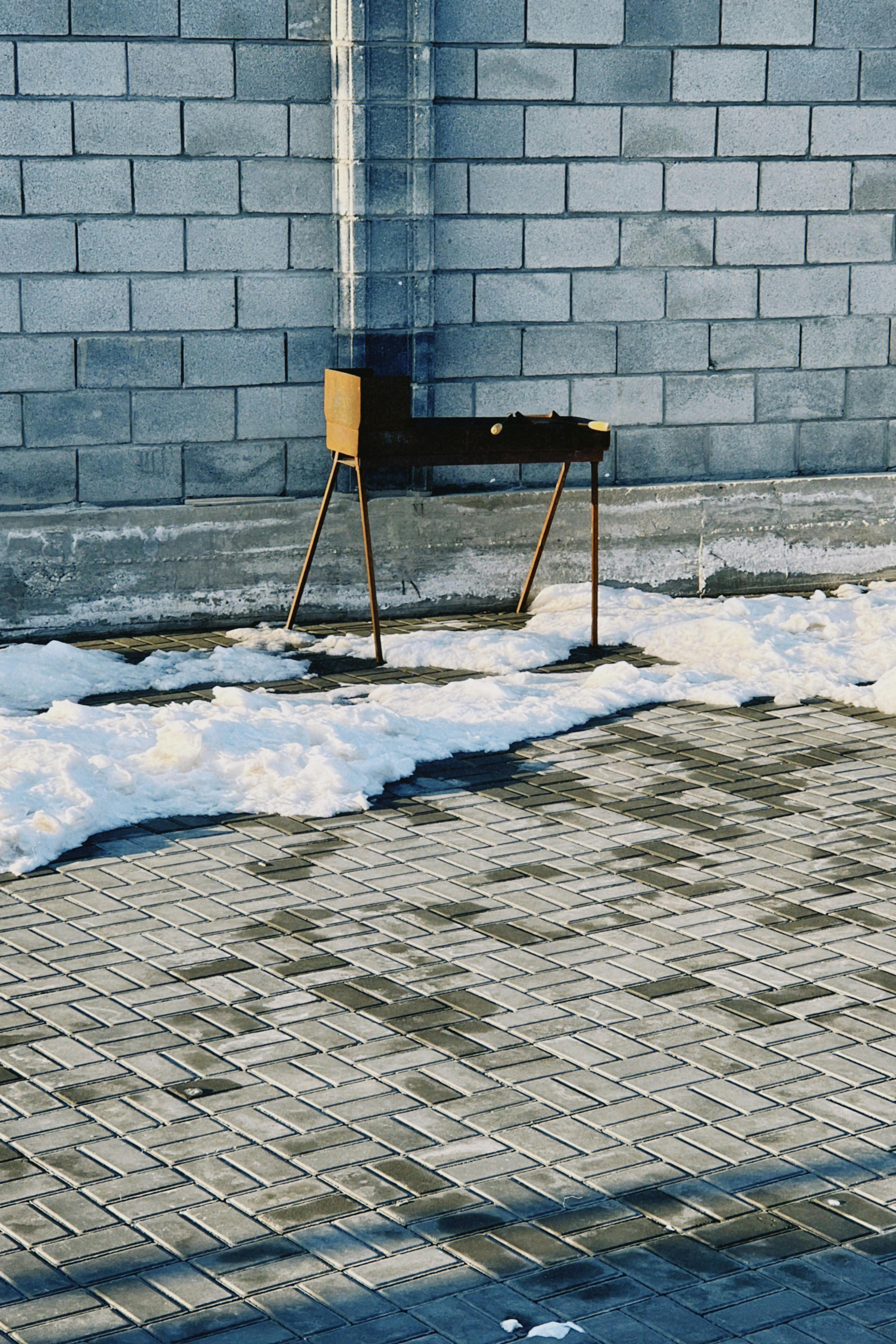 Free A solitary metal grill on a snowy patio against a brick wall on a winter day. Stock Photo