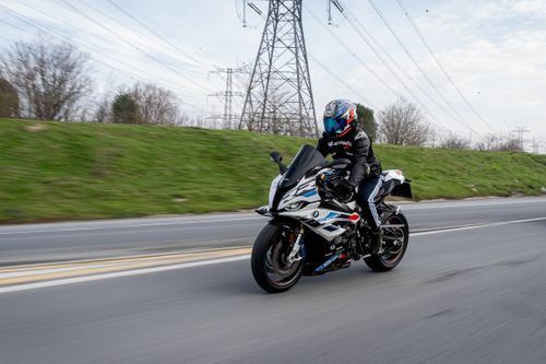 Free A motorcyclist in full gear rides a sports bike on a clear day with power lines and greenery in the background. Stock Photo