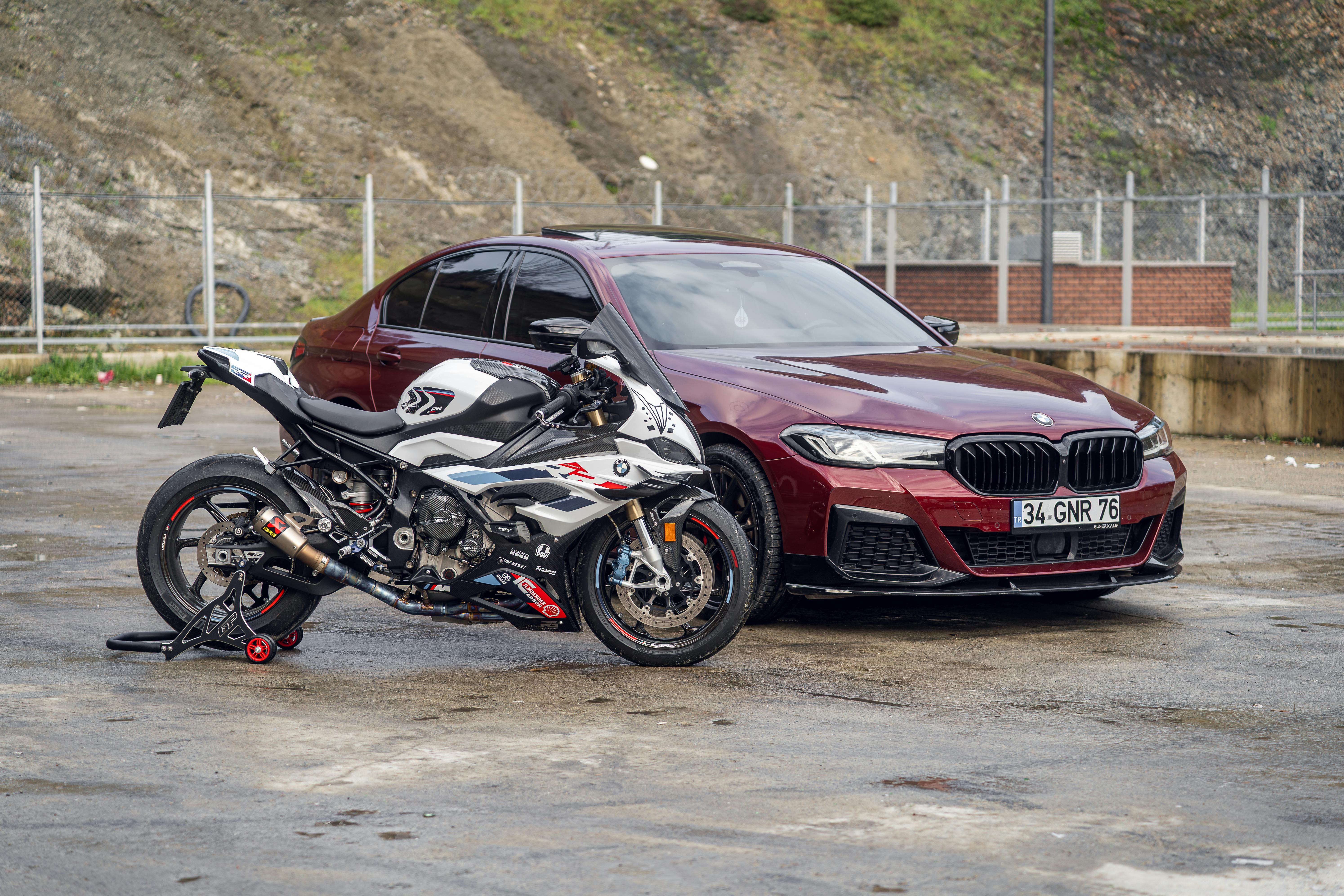 A red sedan and white motorcycle parked outdoors on a wet pavement, showcasing sleek design.