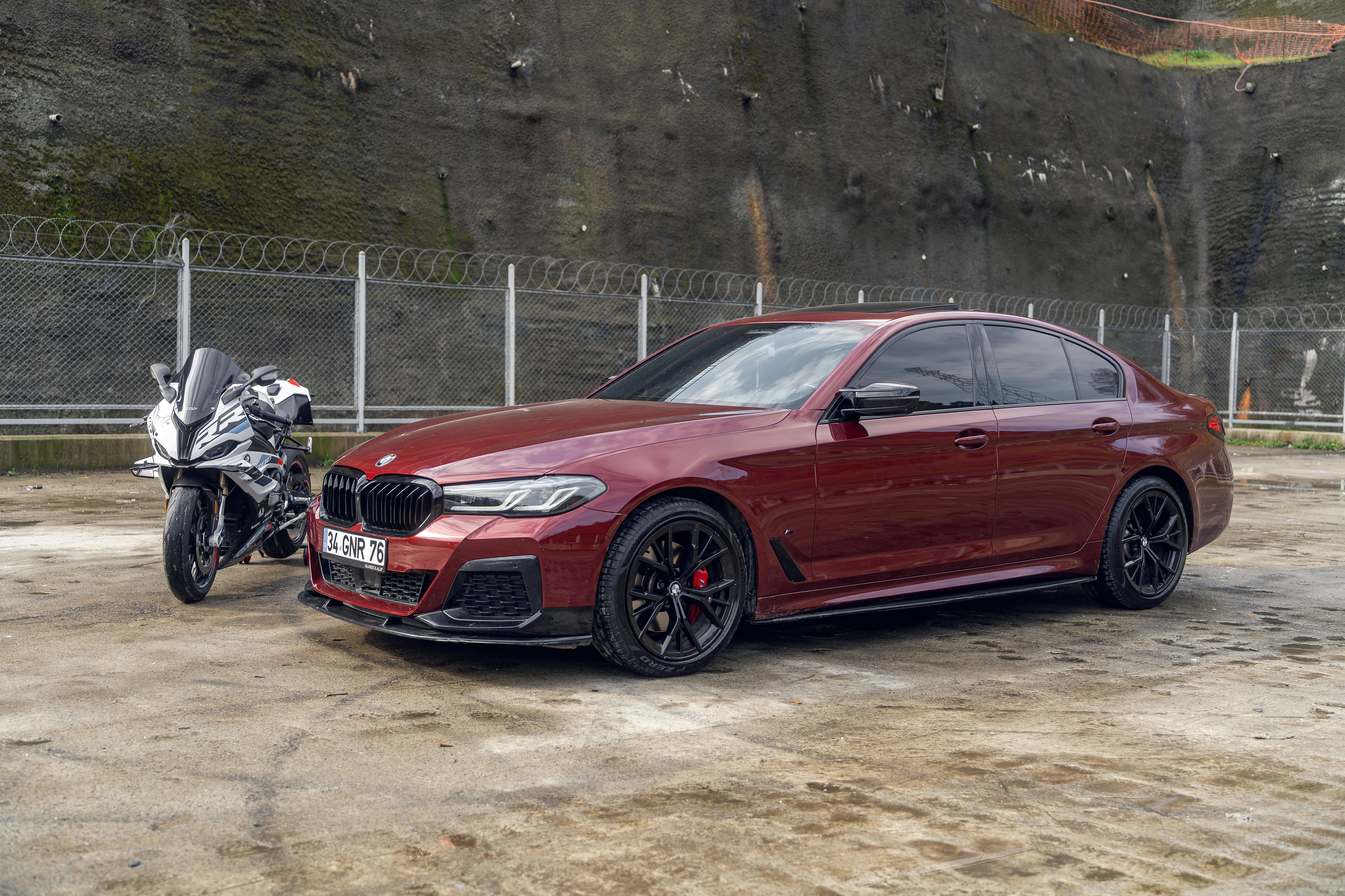 Red BMW sedan parked with a motorcycle in a city area, showcasing luxury and style.