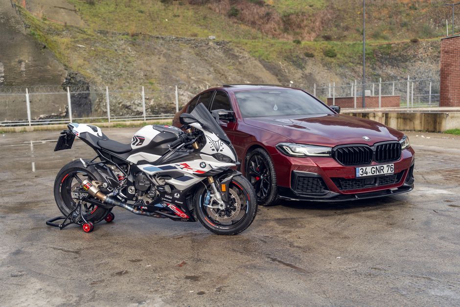 A BMW motorcycle and car parked outside on a rainy day with hills in the background.