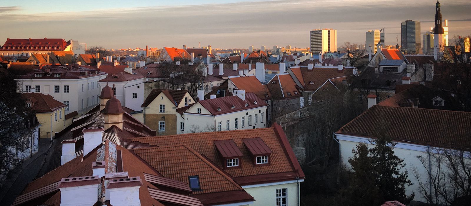 Stunning aerial view of Tallinn's Old Town with red rooftops and modern skyline at sunset.
