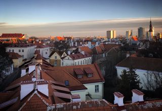 Stunning aerial view of Tallinn's Old Town with red rooftops and modern skyline at sunset.