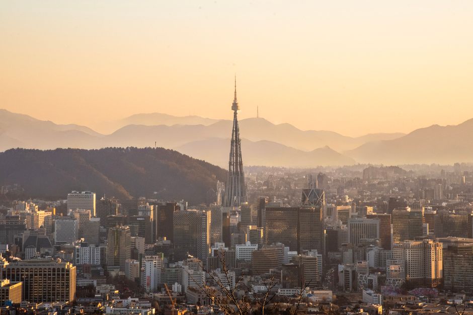 A panoramic view of Seoul's skyline during sunset, featuring Namsan Tower among skyscrapers.