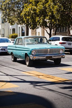 Vintage teal car driving on a sunny street in San Francisco, showcasing urban charm and classic style.