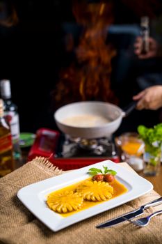 Elegant dessert dish featuring caramelized pineapple served on a vibrant sauce with a chef at work in the background.