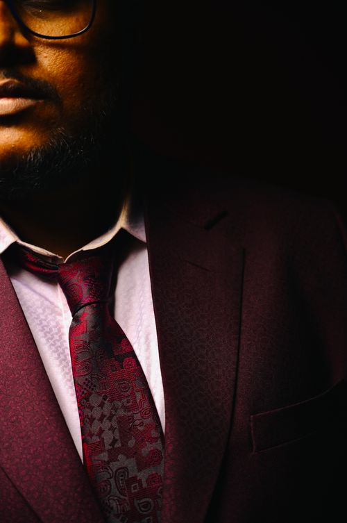 Free Close-up portrait of a well-dressed man in a burgundy suit and tie, captured with dramatic lighting creating a high-contrast effect. Stock Photo