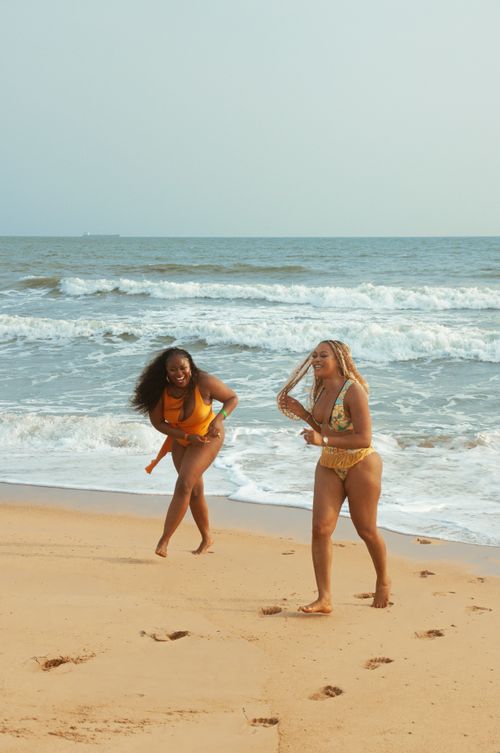 Free Two women laughing and running on a sandy beach by the ocean in colorful swimsuits. Stock Photo