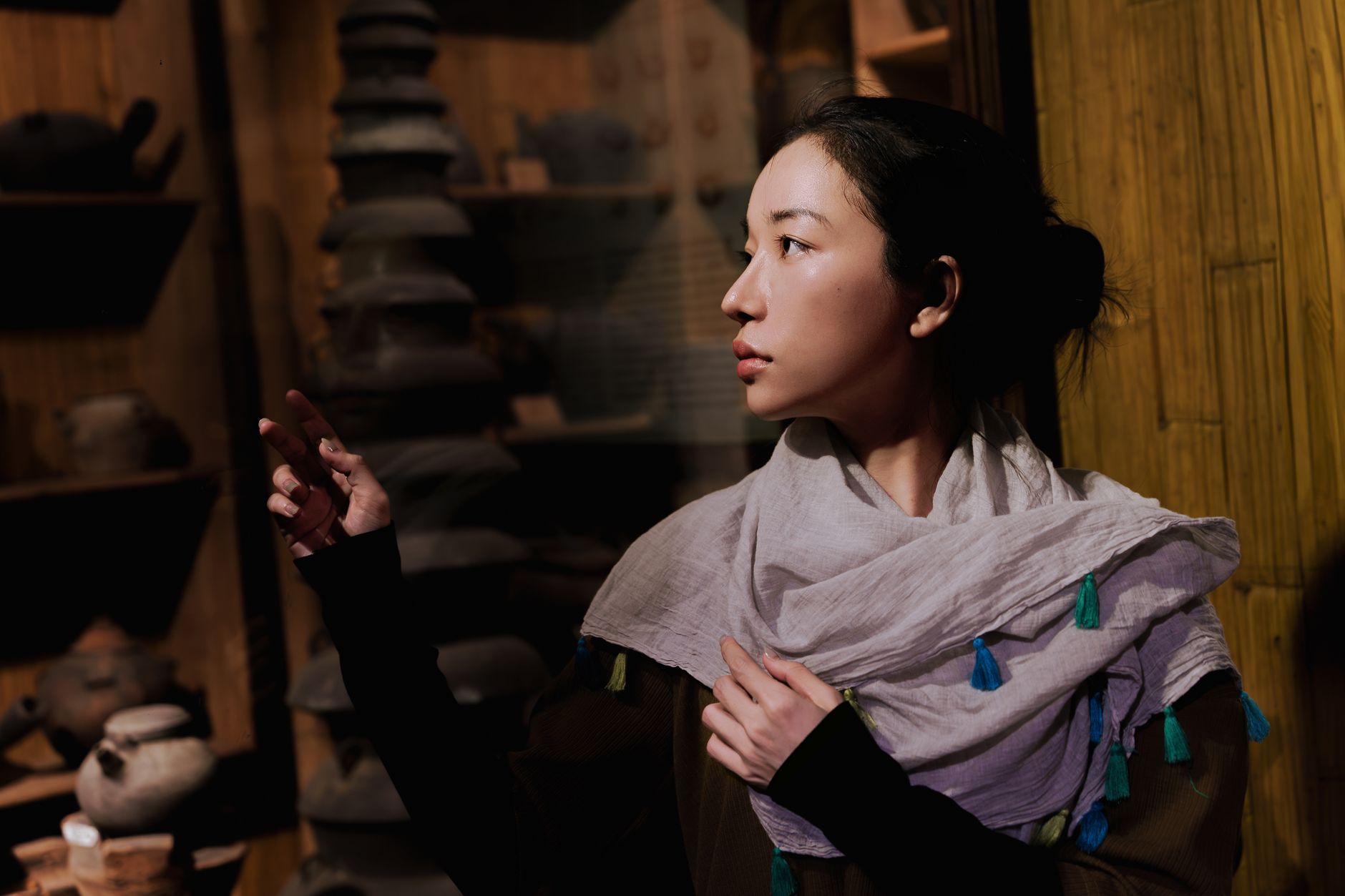 A contemplative woman looks at traditional pottery in a dimly lit museum exhibit in Ho Chi Minh City, Vietnam.