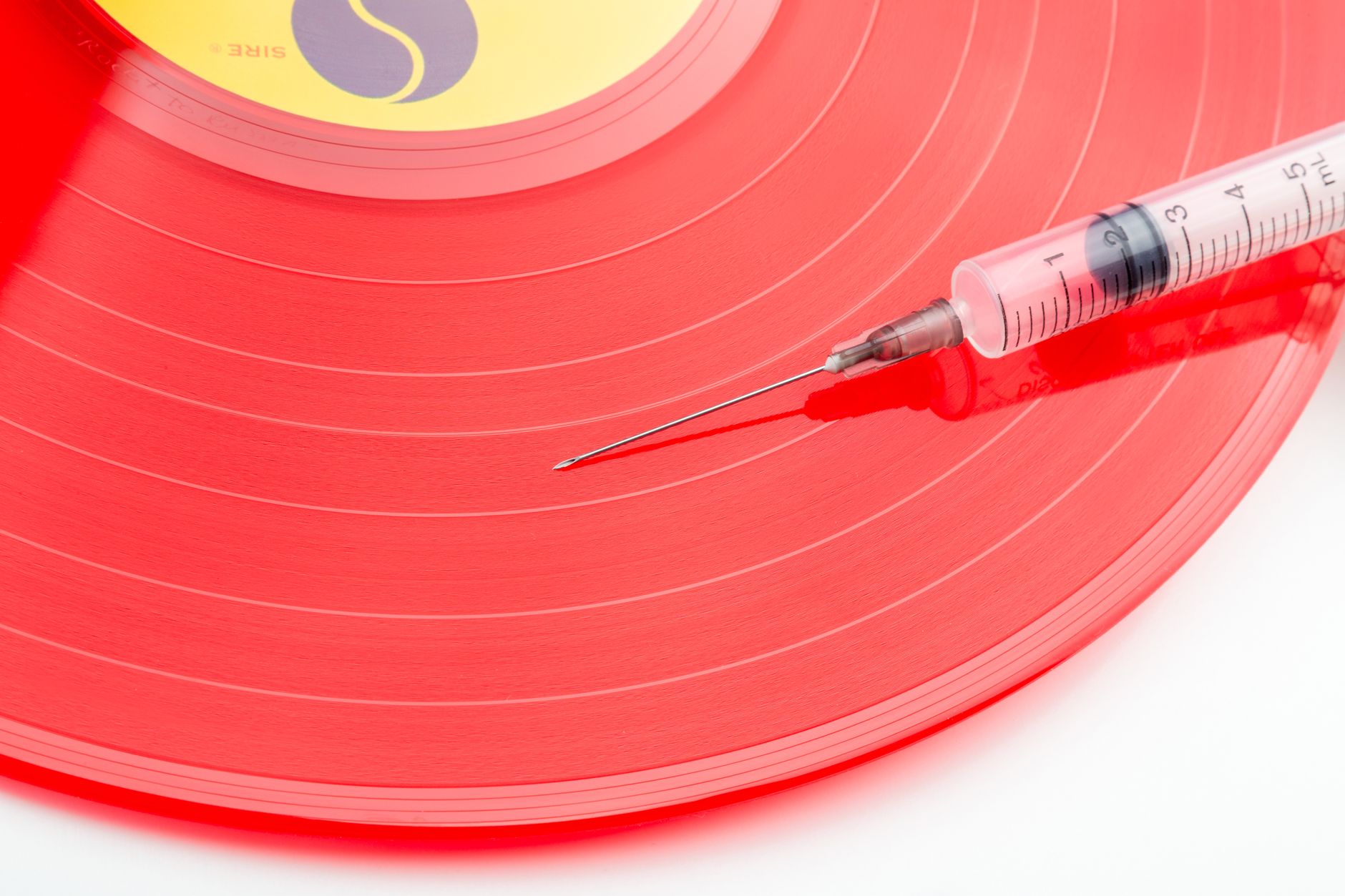 Conceptual image of a red vinyl record with a syringe symbolizing music addiction or nostalgia.