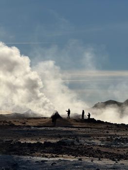 Silhouettes of people at a geothermal field in Iceland with steam rising against a clear sky.