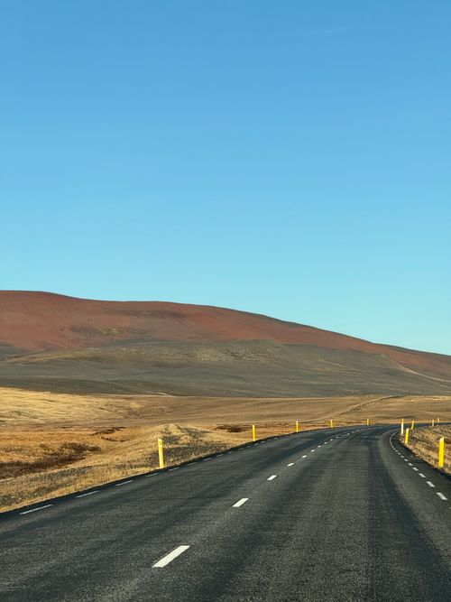 Free Captivating view of an empty road winding through the vibrant Icelandic terrain under a clear blue sky. Stock Photo