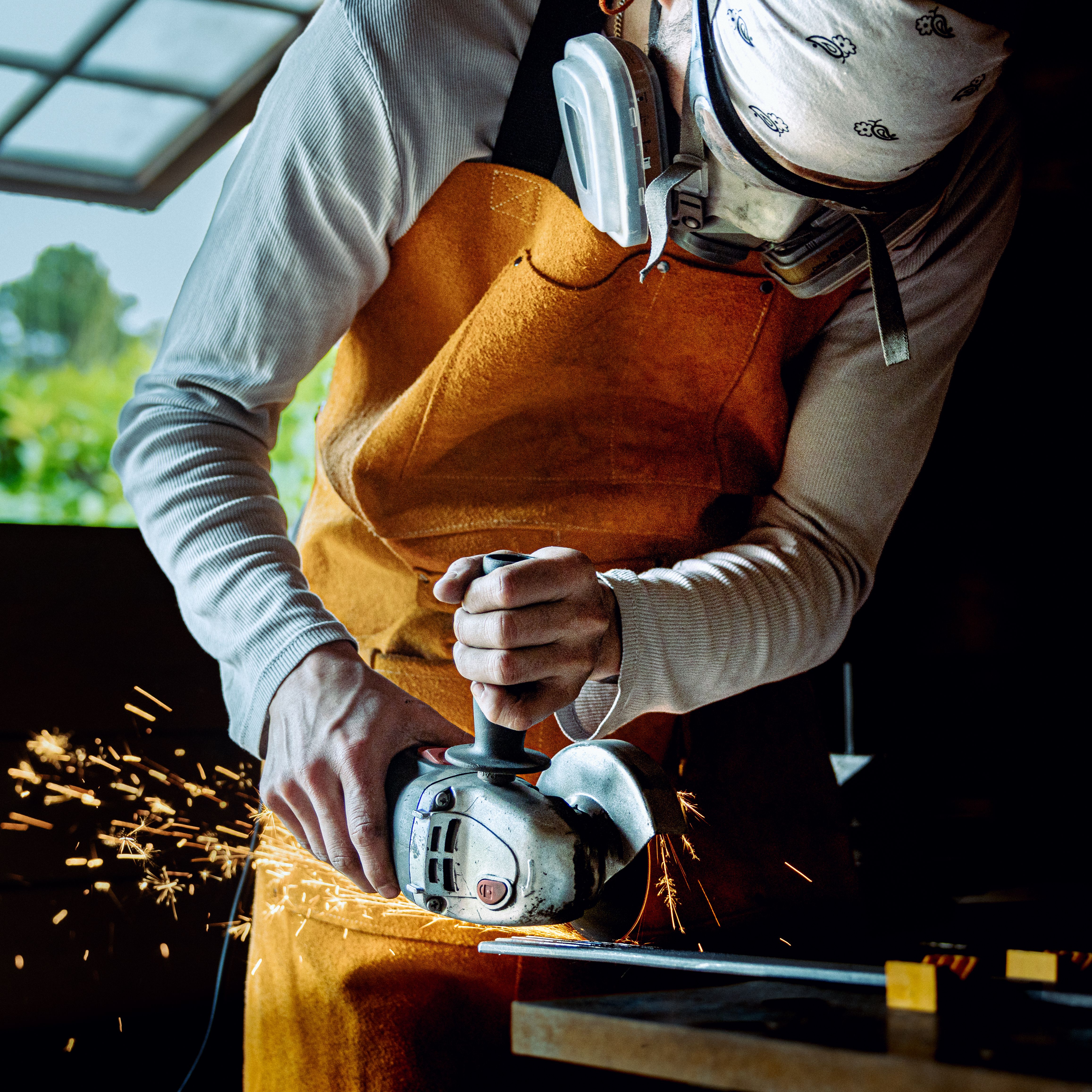 An artisan works with a power tool in a sunlit workshop, creating sparks.
