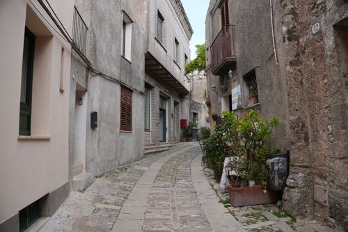 Free Winding cobblestone street in Erice, Sicily lined with historic buildings and lush greenery. Stock Photo