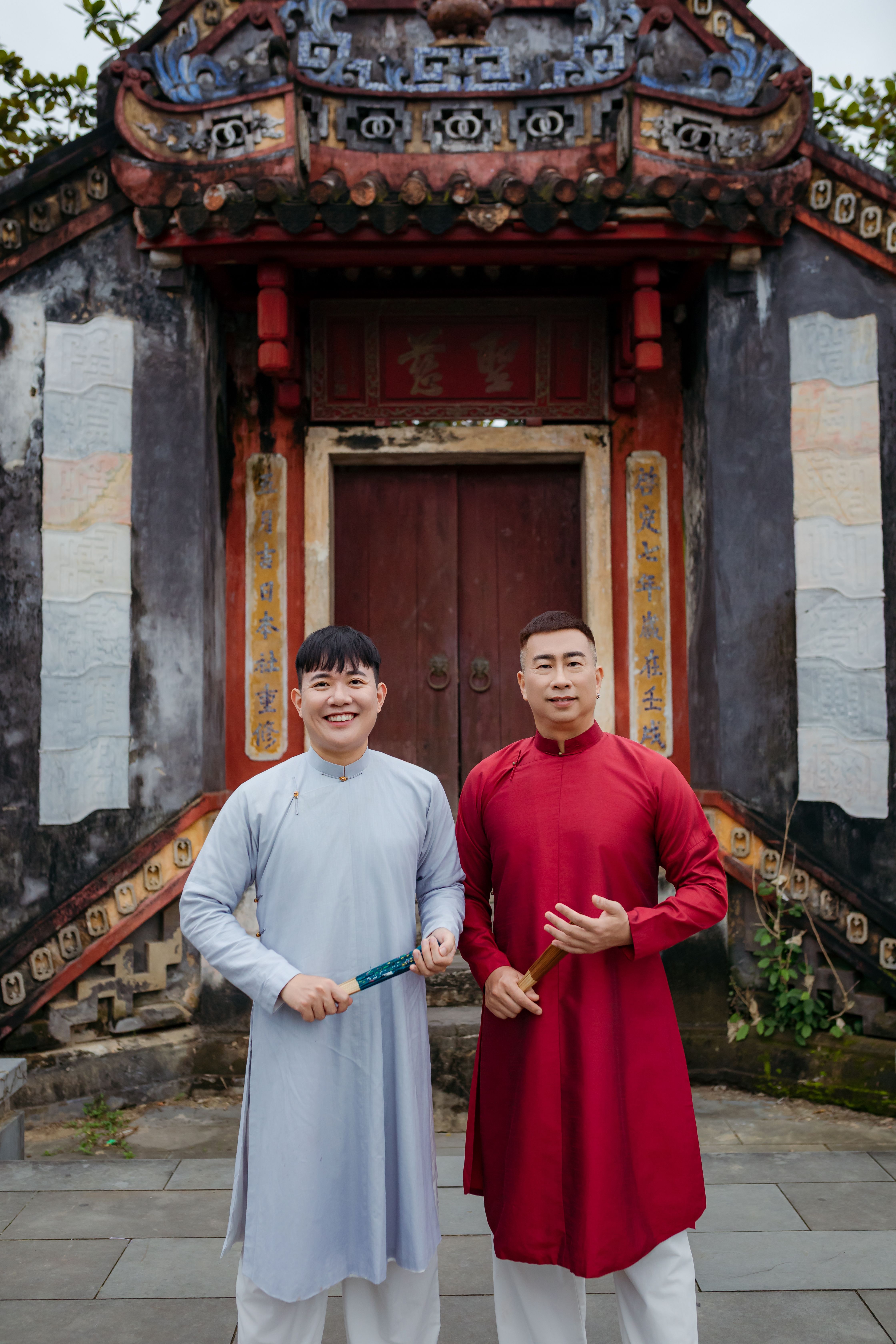 Two men in traditional Vietnamese clothing pose in front of an ancient temple in Hội An, Vietnam.