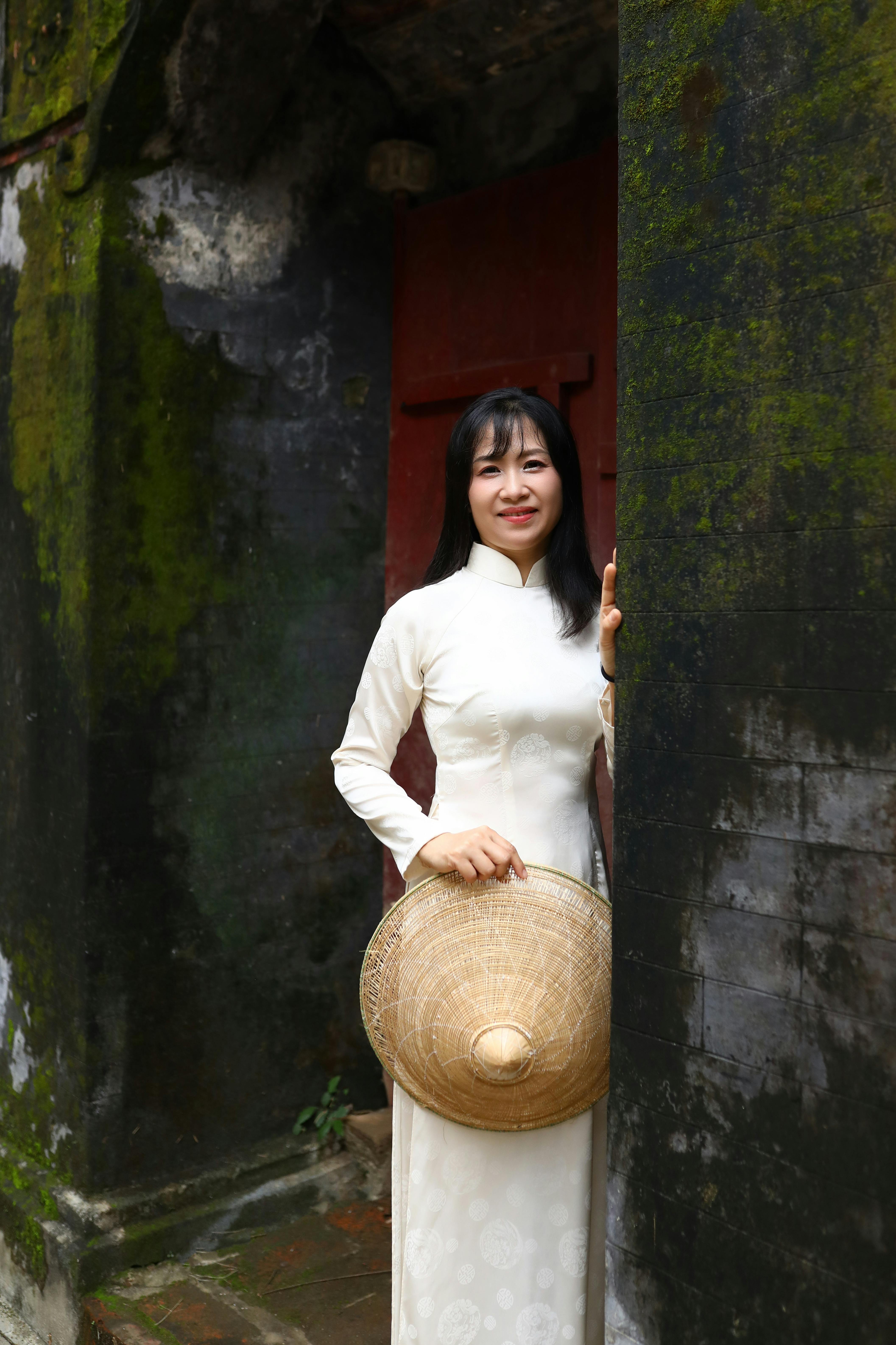 Woman in áo dài holding a conical hat at an ancient wall in Hội An, Vietnam.