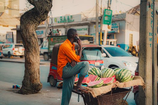A street vendor in Mogadishu sells watermelons while speaking on the phone.