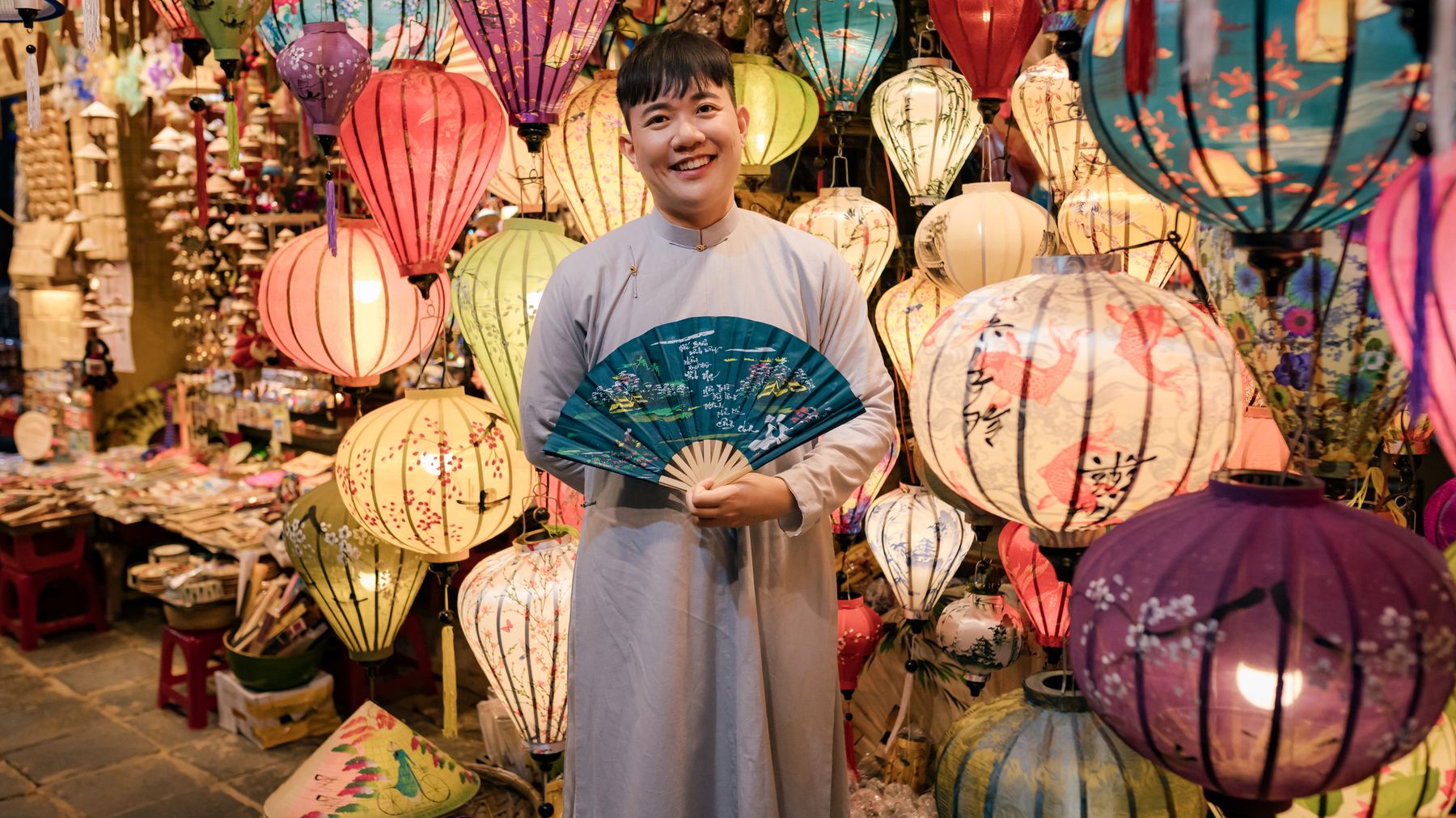 Những chiếc đèn lồng đầy màu sắc ở Hội An cùng một người bán hàng tươi cười trong trang phục truyền thống.