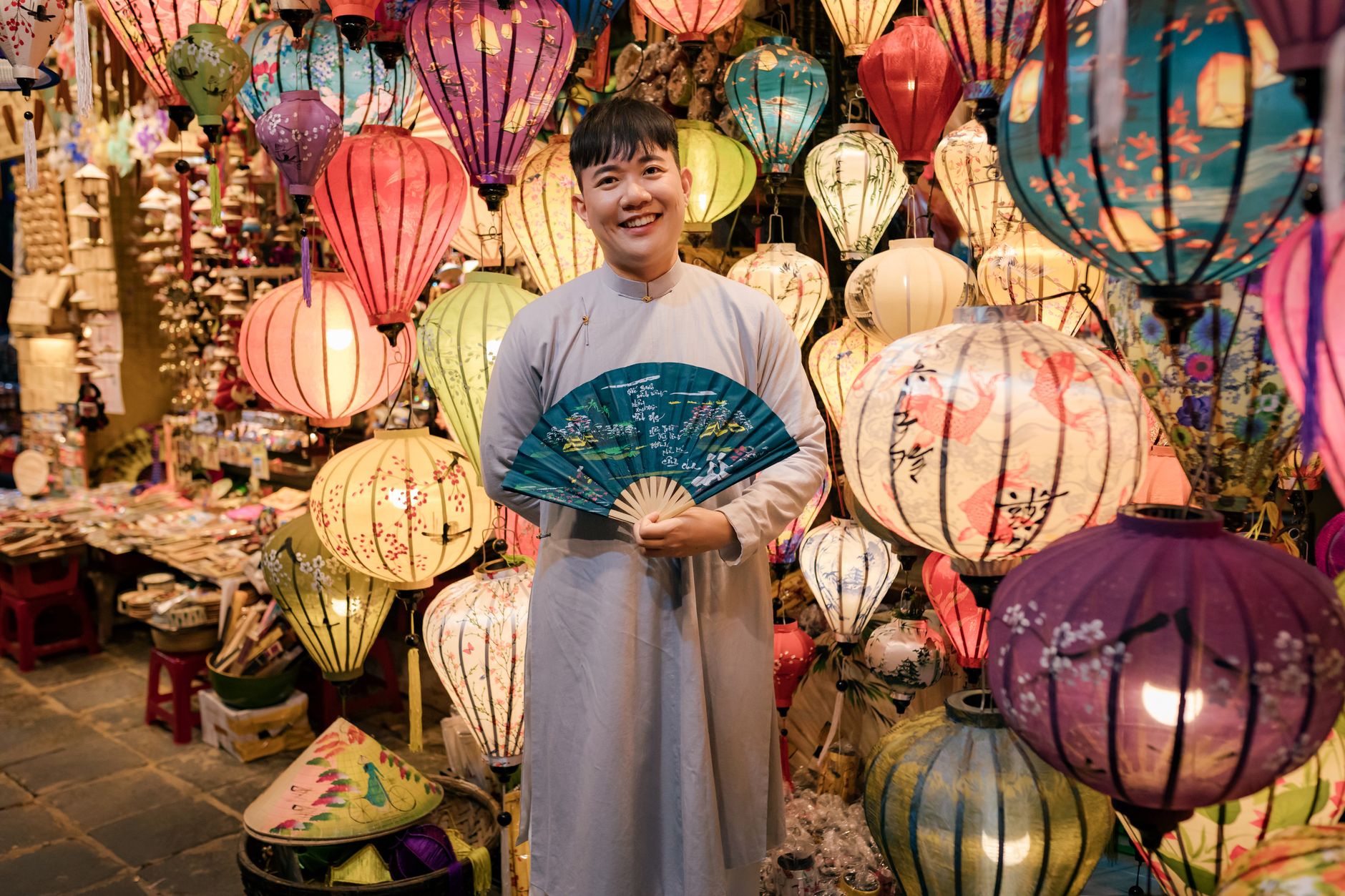 Colorful lanterns in Hội An with a smiling vendor in traditional attire.