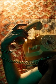 Artistic shot of a rotary phone with a hand on a vintage carpet.
